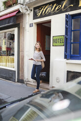 Frankreich, Paris, Porträt einer jungen Frau mit Rollkoffer beim Verlassen eines Hotels - FMKF001350