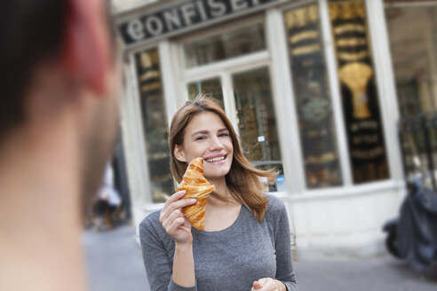 Frankreich, Paris, Porträt einer jungen Frau mit Croissant vor einer Konditorei - FMKF001352
