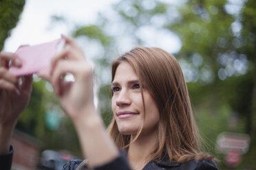 Frankreich, Paris, Porträt einer lächelnden jungen Frau, die mit ihrem Smartphone fotografiert - FMKF001273