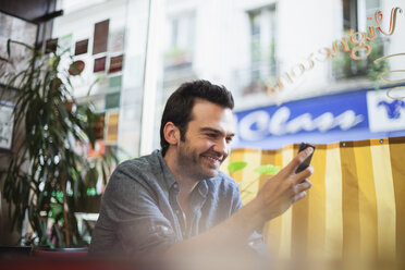 Frankreich, Paris, Porträt eines Mannes, der sein Smartphone in einem Café benutzt - FMKF001277