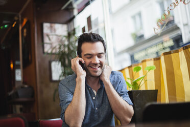 Frankreich, Paris, Porträt eines Mannes, der mit seinem Smartphone in einem Café telefoniert - FMKF001278
