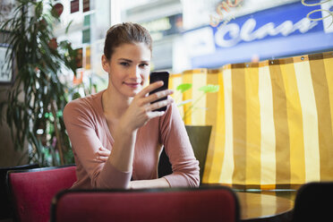 Frankreich, Paris, Porträt einer jungen Frau, die ihr Smartphone in einem Café benutzt - FMKF001280