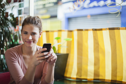 Frankreich, Paris, Porträt einer lächelnden jungen Frau mit ihrem Smartphone in einem Café, lizenzfreies Stockfoto
