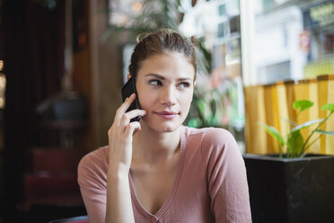 Frankreich, Paris, Porträt einer jungen Frau, die mit ihrem Smartphone in einem Café telefoniert - FMKF001282