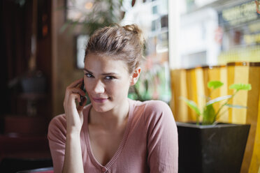 Frankreich, Paris, Porträt einer jungen Frau, die mit ihrem Smartphone in einem Café telefoniert - FMKF001283