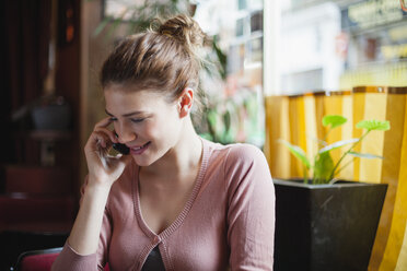 Frankreich, Paris, Porträt einer jungen Frau, die mit ihrem Smartphone in einem Café telefoniert - FMKF001284