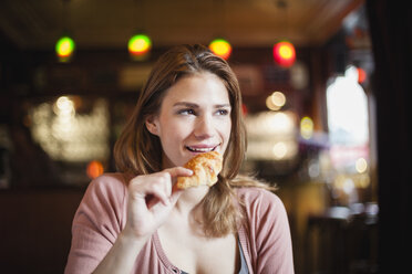 Frankreich, Paris, Porträt einer glücklichen jungen Frau, die in einem Café ein Croissant isst - FMKF001287