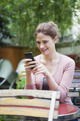 Frankreich, Paris, Porträt einer jungen Frau, die ihr Smartphone in einem Café benutzt - FMKF001290