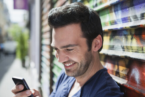 Frankreich, Paris, Porträt eines lächelnden Mannes, der sein Smartphone benutzt - FMKF001296