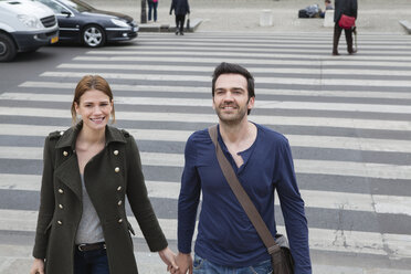 France, Paris, couple walking hand in hand on crosswalk - FMKF001312