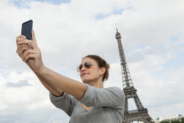 France, Paris, portrait of young woman photographing herself with tablet computer in front of Eiffel Tower - FMKF001333