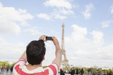France, Paris, man photographing Eiffel Tower with his smartphone, back view - FMKF001334
