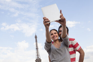 France, Paris, couple photographing themself with tablet computer in front of Eiffel Tower - FMKF001336