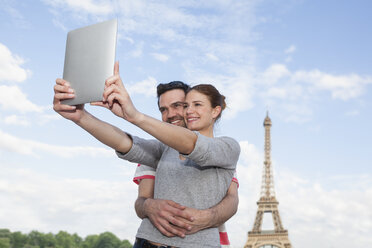 France, Paris, happy couple photographing themself with tablet computer in front of Eiffel Tower - FMKF001338