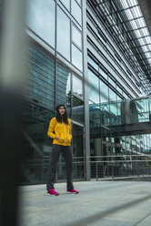 Young woman wearing yellow tracksuit top standing in front of glass front - UUF000985