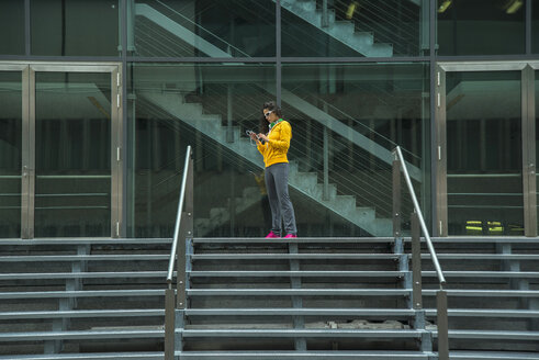 Junge Frau im gelben Trainingsanzug mit Smartphone - UUF000986