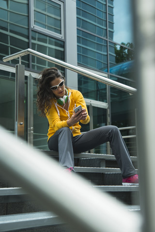 Junge Frau im gelben Trainingsanzug mit Smartphone, lizenzfreies Stockfoto