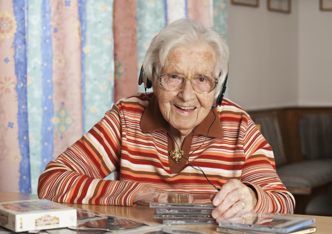 Porträt einer lächelnden älteren Frau, die mit Kopfhörern CDs hört, lizenzfreies Stockfoto