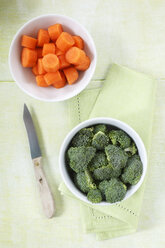 Bowls of broccoli florets and sliced carrots, kitchen knife and cloth on wood - EVGF000692