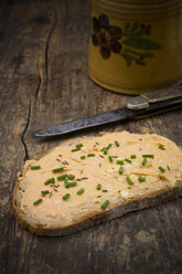 Slice of bread with obazda sprinkled with chives, knife and jar on dark wood - LVF001432