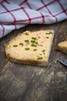 Halbe Scheibe Brot mit Obazda, bestreut mit Schnittlauch und Tuch auf dunklem Holz - LVF001434