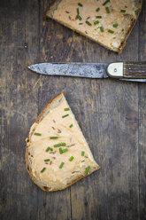 Zwei Hälften einer Brotscheibe mit Obazda, bestreut mit Schnittlauch und Messer auf dunklem Holz - LVF001435