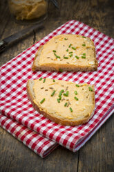 Zwei Hälften einer Scheibe Brot mit Obazda mit Schnittlauch bestreut auf Tuch und dunklem Holz - LVF001438