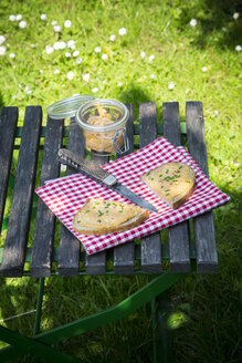 Zwei Brothälften mit Obazda, bestreut mit Schnittlauch, Tuch, Messer und Einmachglas auf dem Gartentisch - LVF001443