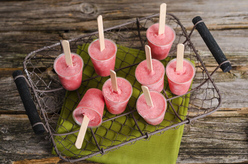 Wire basket of home-made strawberry ice lollies on cloth and wood - ODF000735