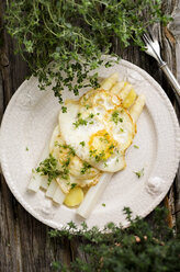 Teller mit zubereitetem weißen Spargel mit Kartoffeln, Spiegelei und Kräutern auf Holz - ODF000745