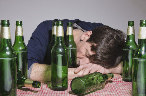 Mann auf Tisch liegend, umgeben von Bierflaschen - MUF001515
