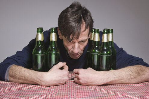 Mann am Tisch, umgeben von Bierflaschen - MUF001508
