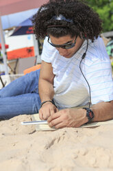 Junger Mann mit digitalem Tablet hört Musik am Strand - VTF000298