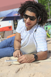 Portrait of a young man with digital tablet listening music on the beach - VTF000299