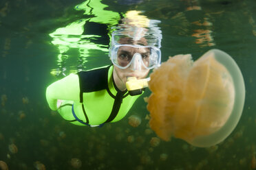 Oceania, Palau, Eik Malk, Female snorkeller watching spotted jellyfish, mastigias papua, in saltwater lake - FGF000030