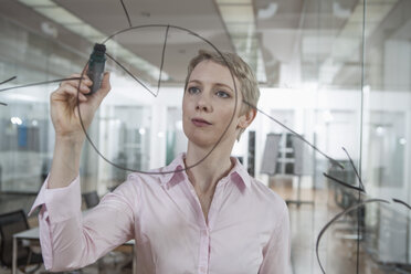 Germany, Munich, Businesswoman in office, drawing chart on glass pane - RBYF000515