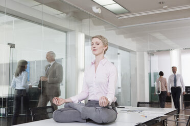 Germany, Munich, Businesswoman in office, meditating on desk - RBYF000580
