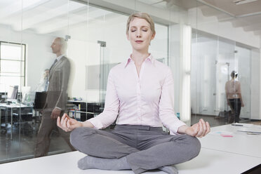 Germany, Munich, Businesswoman in office, meditating on desk - RBYF000582