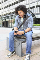 Young male student sitting on bench using his smartphone - VTF000289