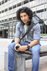 Junger männlicher Student sitzt auf einer Bank und benutzt sein Smartphone - VTF000290