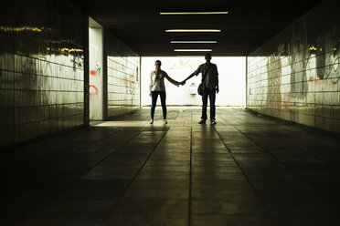 Young couple standing hand in hand in a dark underpass - UUF001096