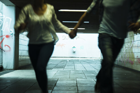 Young couple running hand in hand in a dark underpass, partial view - UUF001073