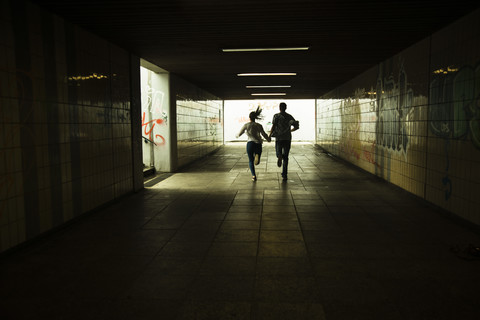 Young couple running hand in hand in a dark underpass, partial view stock photo