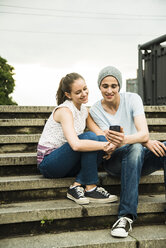 Junges Paar mit Smartphone auf einer Treppe sitzend - UUF001086