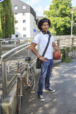 Junger männlicher Student mit Basketball neben seinem Rennrad stehend, lizenzfreies Stockfoto