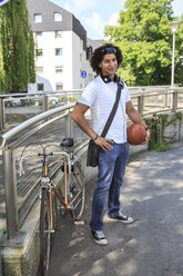 Junger männlicher Student mit Basketball neben seinem Rennrad stehend - VTF000291