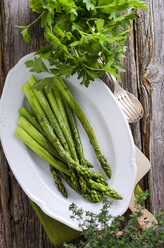 Teller mit gedämpftem grünem Spargel, Asparagus officinalis, und Petersilie auf Holz - ODF000764