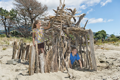 Neuseeland, Golden Bay, Pakawau, Mädchen und Junge am Strand bauen ein Haus aus Treibholz, lizenzfreies Stockfoto