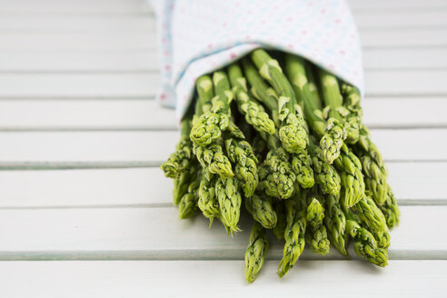 Bündel grüner Spargel, Asparagus officinalis, in ein Tuch eingewickelt, auf weißem Holz liegend - LVF001460