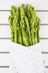 Bunch of green asparagus, Asparagus officinalis, wrapped in cloth lying on white wood - LVF001446